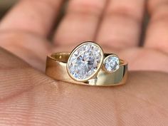 a close up of a person's hand holding a gold ring with two diamonds