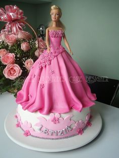 a barbie doll cake with pink and white frosting on the top, surrounded by roses