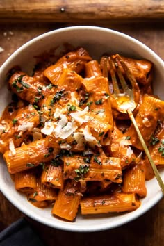 a white bowl filled with pasta and sauce on top of a wooden table next to a fork