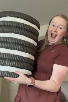 a woman holding a giant stack of black and white tires with her mouth wide open