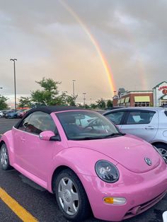 a pink convertible car parked in a parking lot under a rainbow