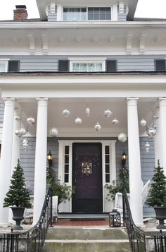 the front porch of a house decorated for christmas with ornaments hanging from the roof and wreaths on the columns