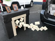 a table with cards and pictures on it next to a parked car in a parking lot