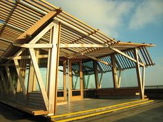 a wooden structure sitting on top of a parking lot next to the ocean with lots of windows