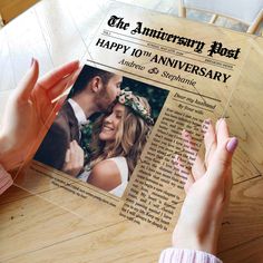 a person holding up an anniversary card on top of a wooden table next to a woman's hand