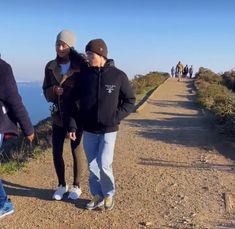 three people walking along a path near the ocean