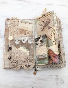 an altered book with lace, buttons and other things on it's cover sitting on a white wooden surface