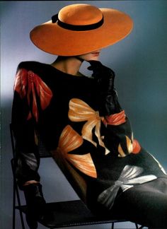 a woman sitting on a chair wearing a large orange hat and black dress with flowers