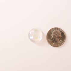 a penny and a small glass bead on a white surface with a coin in the background