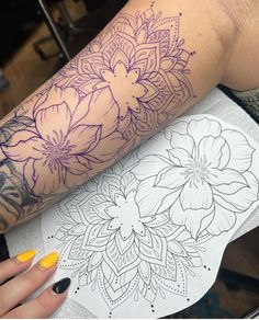 a woman's arm with flowers on it and a coloring book next to her