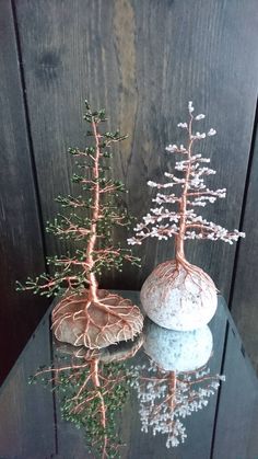 two small trees sitting on top of a table next to rocks and plants in vases