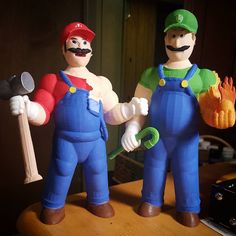 two toy figurines that are standing on a table with one holding a hammer and the other wearing overalls