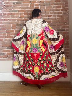 a woman is standing in front of a brick wall and wearing a colorful jacket with flowers on it