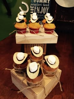 several cupcakes with hats on them sitting on a wooden box in front of a sign