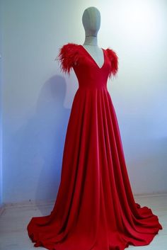 a red dress with feathers on it is displayed in front of a white wall and floor