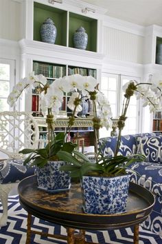 a living room with blue and white furniture and flowers in vases on the coffee table