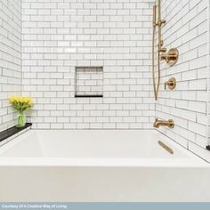 a white tiled bathroom with gold fixtures and yellow flowers in the bathtub, along with brass faucets