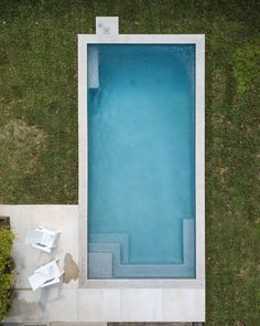 an aerial view of a swimming pool in the middle of a lawn with chairs around it