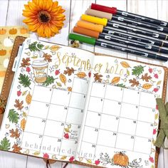 an open planner with autumn leaves and pumpkins next to some crayon markers