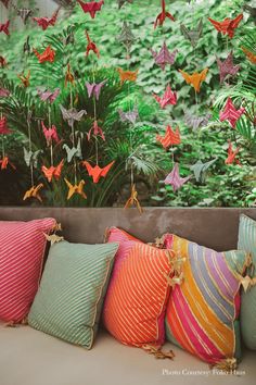 many colorful pillows are lined up in front of a wall with origami cranes hanging from it