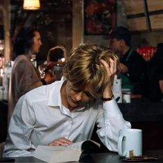 a man sitting at a table with his head in his hands and reading a book