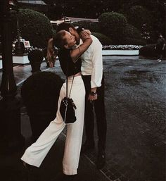 a man and woman kissing on the street in front of a lamp post at night