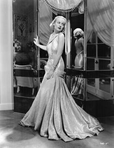 an old photo of a woman in a dress standing next to a glass case with mannequins behind it