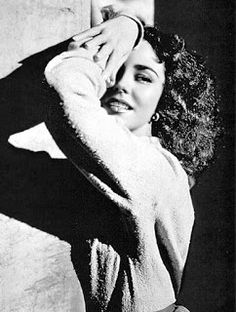 a black and white photo of a woman leaning against a wall with her hands on her head