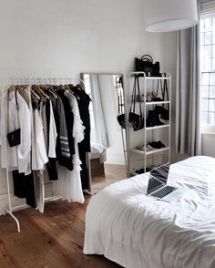 a white bed sitting next to a closet filled with clothes and handbags on hangers