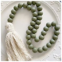 a white plate topped with green beads next to a tasseled beaded necklace