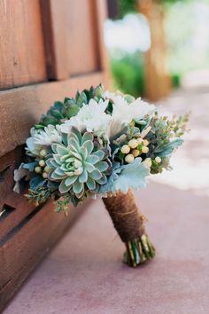 a bridal bouquet sitting on the side of a wooden bench with succulents