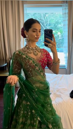 a woman in a green sari taking a selfie with her cell phone while sitting on a bed