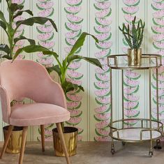 a pink chair next to a potted plant in front of a wallpaper