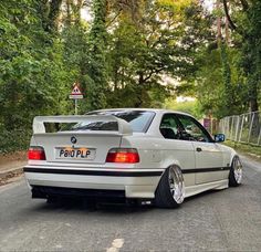 a white car parked on the side of a road next to some trees and bushes