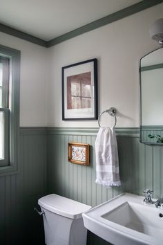 a white toilet sitting next to a bathroom sink under a framed picture on the wall