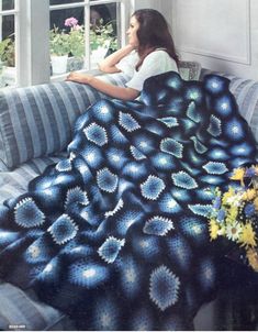 a woman sitting on a couch under a blue and white blanket in front of a window