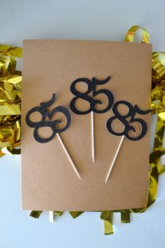 three black cake toppers sitting on top of a brown card next to gold foil