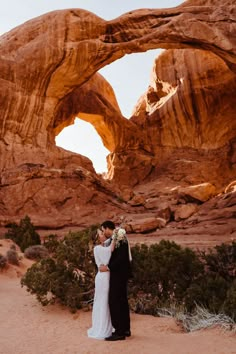 a bride and groom standing in front of an arch rock formation at their desert wedding