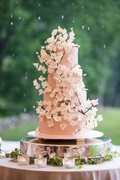 a pink wedding cake with white flowers on top and candles in the middle, sitting on a round table