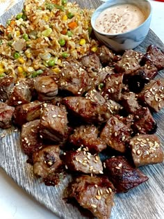 a plate with meat, rice and sauces on it next to a bowl of dipping sauce