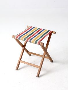 a small wooden stool with multi - colored stripes on it's seat cover, against a white background