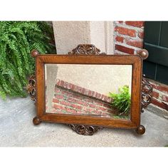 a mirror sitting on the ground next to a brick wall and green plant in it