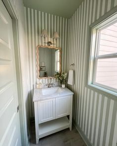 a white sink sitting under a bathroom mirror next to a window in a room with striped walls