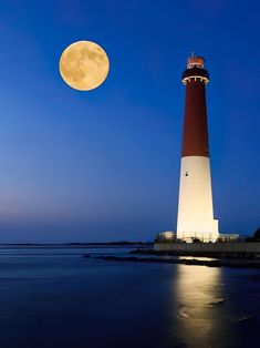 a full moon is seen above the lighthouse