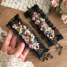 two black lace garters with pink and blue flowers on them, one being held by a woman's hand