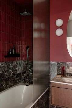 a bathroom with red walls and marble counter tops, along with a white bathtub