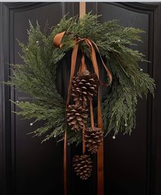 a wreath with pine cones and ribbons hanging from it's side on a door