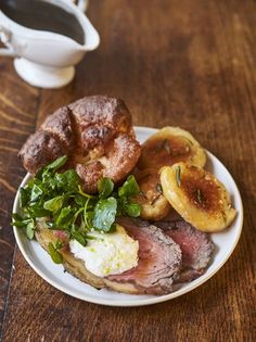 a white plate topped with meat, potatoes and greens next to a cup of coffee