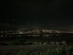 the city lights shine brightly in the dark night sky over water and rocks on the shore