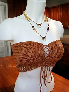 a white mannequin wearing a brown top with gold chains and beads on it